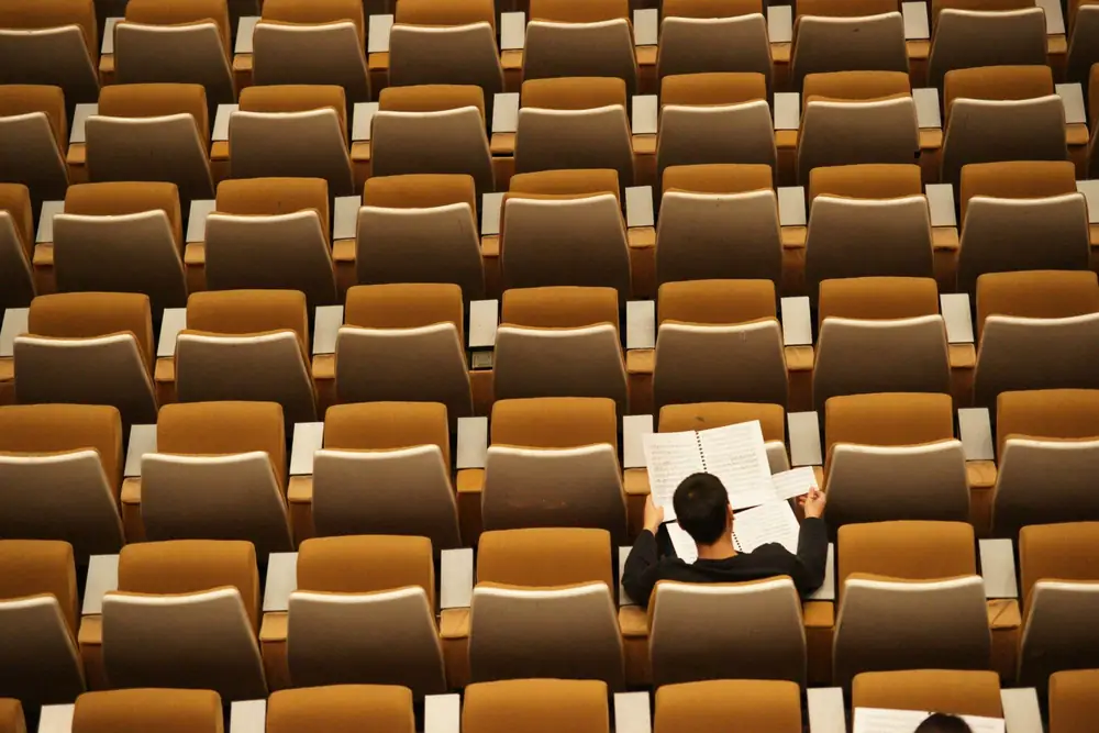 Student reading papers alone in a large lecture hall with rows of empty seats